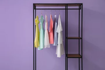 Tuinposter Shelving unit with children's dresses near lilac wall © Pixel-Shot