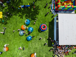 ariel view of playground with children playing in zorb balls with parents on green grass