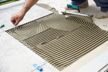 The hands of the tiler are laying the ceramic tile on the floor.