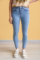 Young woman in stylish jeans near yellow wall