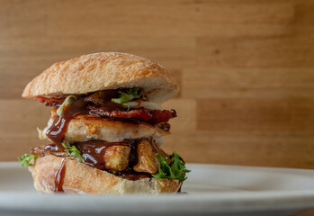 Delectable combination of a chicken burger accompanied by bacon, crispy potato wedges, a savory brown sauce, and a refreshing green salad.