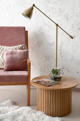 Pink armchair with cushions, lamp and florarium on coffee table near white grunge wall