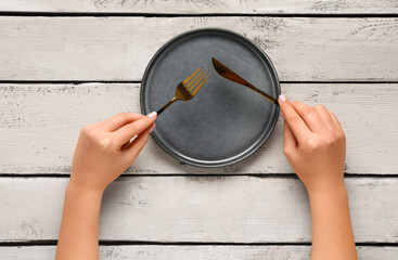 Woman holding fork and knife near clean plate on white wooden table - Powered by Adobe