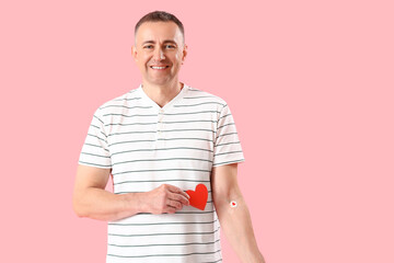 Fototapeta Mature blood donor with applied medical patches and paper heart on pink background obraz