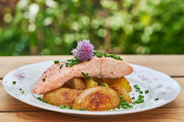 Poached or steamed salmon fillet served with baked new poptatoes and chopped chives on the rustic porcelain plate outside in the garden restaurant. Low calories, healthy dish ideal for balanced diet.