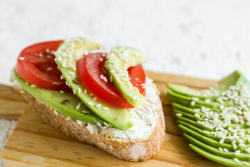 Wooden board of tasty bruschetta with avocado and tomatoes on light background, closeup