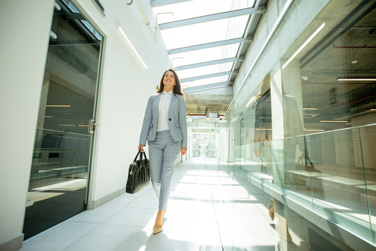 Pretty young business woman walking with briefcase in the office hallway - Powered by Adobe