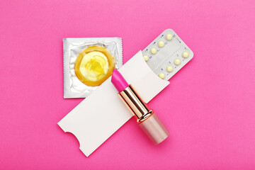 Oral contraceptive pills with condom and lipstick on pink background