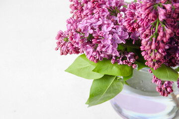 Vase with bouquet of lilac flowers on light background, closeup