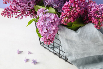 Basket with beautiful lilac flowers on light table, closeup