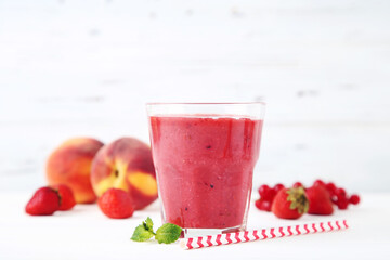 Red smoothie in glass with fruits on white wooden background