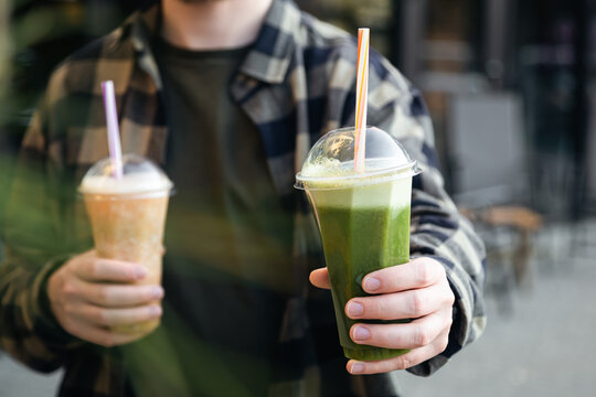 A man outdoors holds a plastic glass with a green banana and mint smoothie, a delicious cooling summer drink.