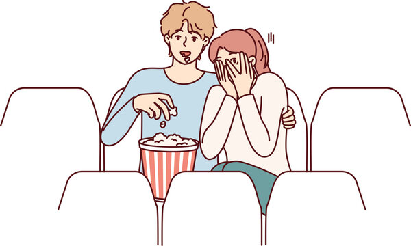 Guy and girl are watching horror movie in cinema and eating popcorn enjoying films about vampires
