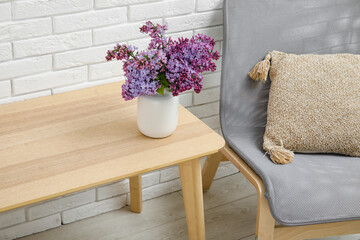 Vase with beautiful lilac flowers on wooden table near light brick wall