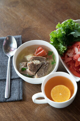 Clear meat soup with potatoes carrot and onion in white bowl on wooden table. Asian style food