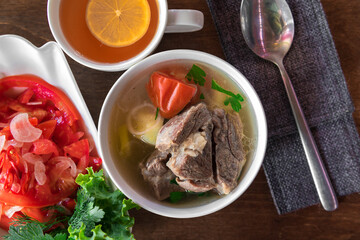 Clear meat soup with potatoes carrot and onion in white bowl on wooden table. Asian style food