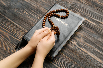 Female hands with prayer beads and Holy Bible on wooden background