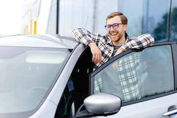 Great Car. Cheerful guy standing near autoand smiling, buying vehicle in dealership center