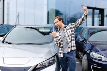 Happy man taking selfie through smart phone after purchasing new car. The man showing the purchased...