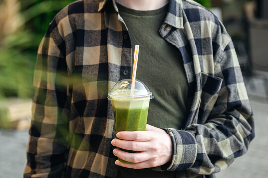 A man outdoors holds a plastic glass with a green banana and mint smoothie, a delicious cooling summer drink.