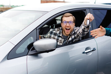 Excited young man showing a car key, sitting inside his new vehicle