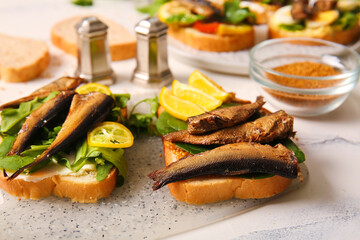 Board of tasty sandwiches with canned smoked sprats on table