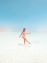 Beautigul girl in swimming suit on Dead sea salt crystals formation coastline, clear cyan green water at Ein Bokek beach, Israel