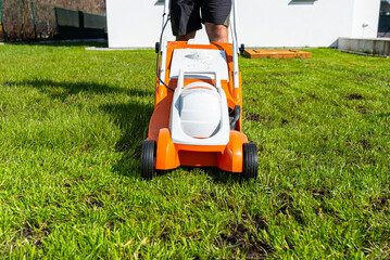 A man mows the grass with an orange electric mower.