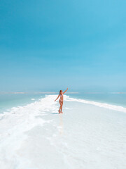 Fototapeta na wymiar Beautigul girl in swimming suit on Dead sea salt crystals formation coastline, clear cyan green water at Ein Bokek beach, Israel
