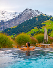 Man in outdoor infinity pool with snowy mountain in the background. Family vacation in luxury...
