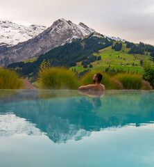 Fototapeta na wymiar Man in outdoor infinity pool with snowy mountain in the background. Family vacation in luxury Alpine resort. Kids in the Alps mountains.