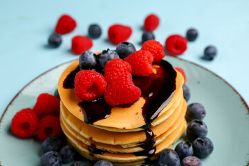 Plate with sweet pancakes and berries on blue background, closeup