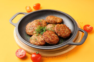 Frying pan with cutlets, dill and tomatoes on yellow background