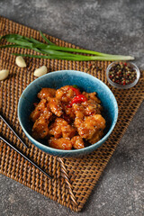 Tasty sweet and sour chicken in bowl with spices on grey background