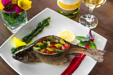 The Baked trout stuffed with vegetables on a plate with some white wine near on wooden table