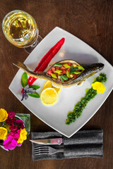 The Baked trout stuffed with vegetables on a plate with some white wine near on wooden table