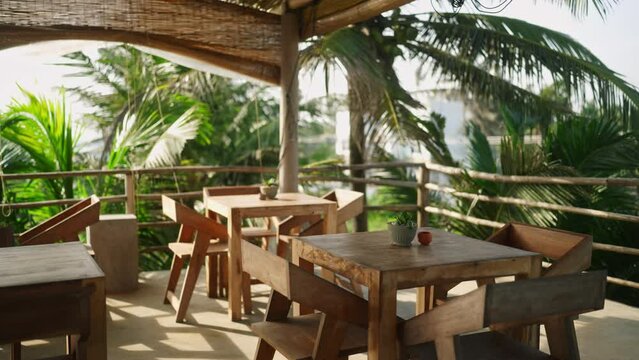 Empty tropical rooftop cafe by the sea at resort waiting for guests and clients. Authentic restaurant at exotic location with wooden chairs and tables, no people on sunny day. Summer vacation concept