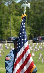 Anonymous Police officer holding the American flag at a veterans cemetery with american flags in the background
