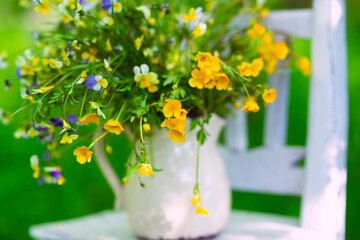 Bouquet of summer wild flowers in a ceramic jug on an old chair in the garden. Vintage summer photo.
