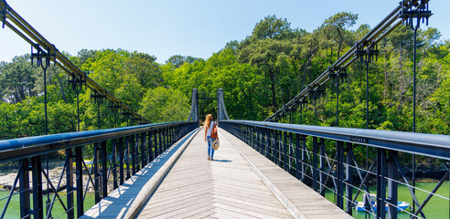 Woman tourist walking on supended bridge in Breton village- le Bono