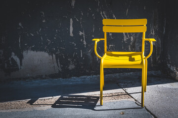 Yellow modern garden chair in front of old concrete wall, high contrasts of sun and shadow, modern...