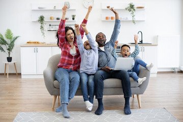 Emotional multiracial people raising arms high in air while watching online football match on...