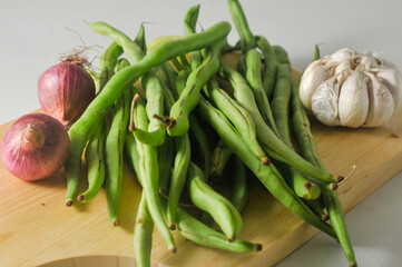 Some green beans, some red onions and a garlic bulb on a wooden chopping board isolated on a white background