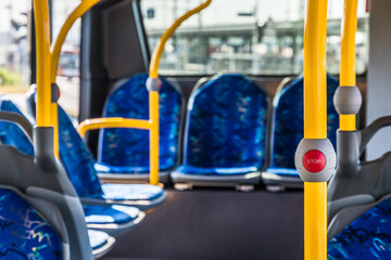 Stop button on the modern public transport bus. Empty bus interior. Public transport in the city. Passenger transportation. Bus with blue seats and yellow handrails.