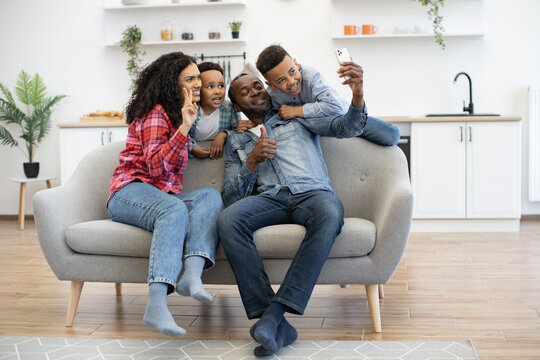 Full length view of african american parents giving thumb up and V sign while taking photo on smartphone with two boys. Cheerful adults and children saving happy moments of pastime together.