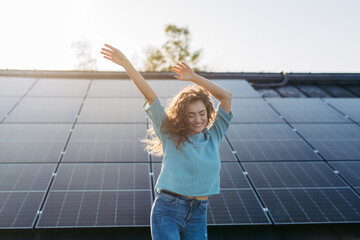 Portrait of young excited woman on roof with solar panels.