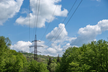A high-voltage tower with wires among the trees against a cloudy blue sky.