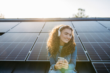 Portrait of young excited woman on roof with solar panels, listening music.