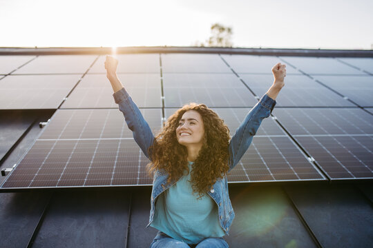 Portrait of young excited woman on roof with solar panels.