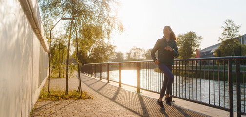 Athletic young woman in activewear running along the embankment of river.